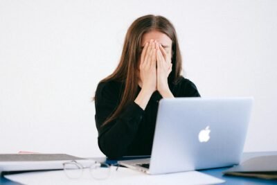 Woman sitting in front of macbook with hands over her face.