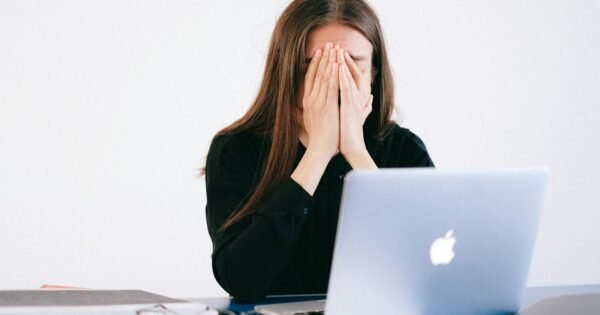 Woman sitting in front of macbook with hands over her face.