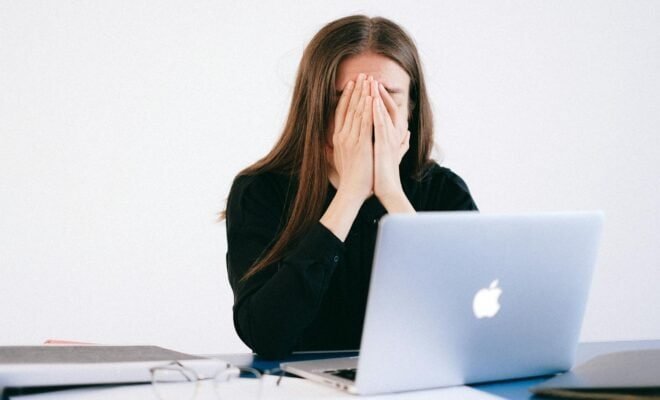 Woman sitting in front of macbook with hands over her face.