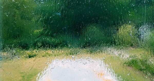A path leading to a gathering of trees who leaves are bright and green. The scene is obscured by a layer of rain as if the viewer is looking out a window