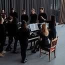 group of people standing around a piano with a choir director