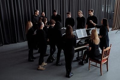group of people standing around a piano with a choir director