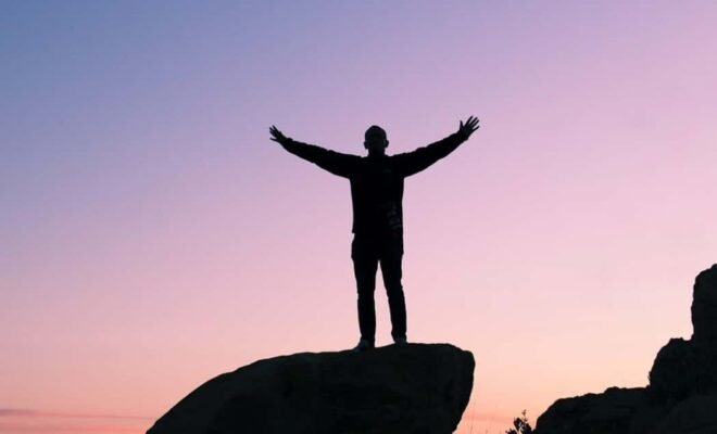 person with open arms in gratitude on a mountain at sunset