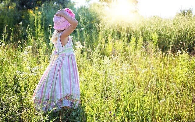 little girl in pink hat standing in field of grass