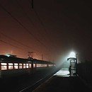 A passenger train and a lone figure at a train station at night.