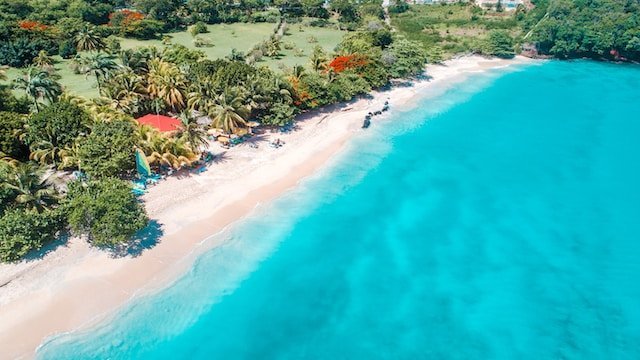 White sand and crystal-blue beach with palm trees and cottages in Grenada