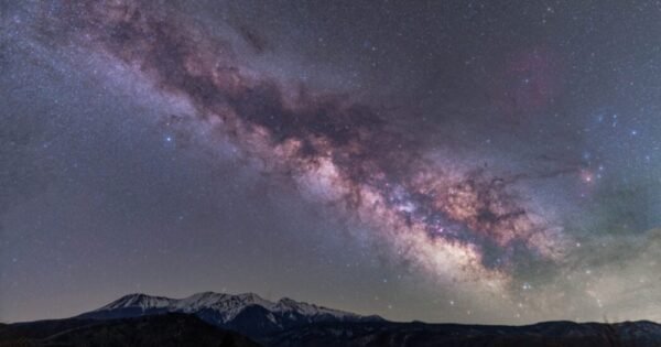 An arm of the Milky Way stretches across a field of stars, creating cloudy stripes of purple