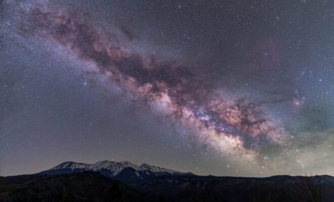 An arm of the Milky Way stretches across a field of stars, creating cloudy stripes of purple