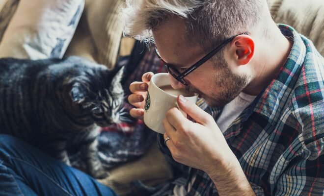 image of a man drinking coffee on a sofa with cat