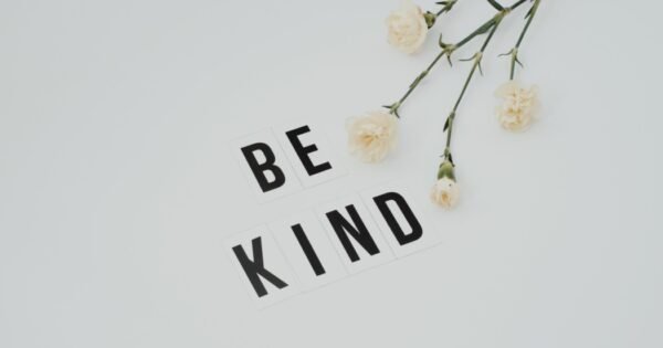 the words be kind in black print on a white background next to cut flowers