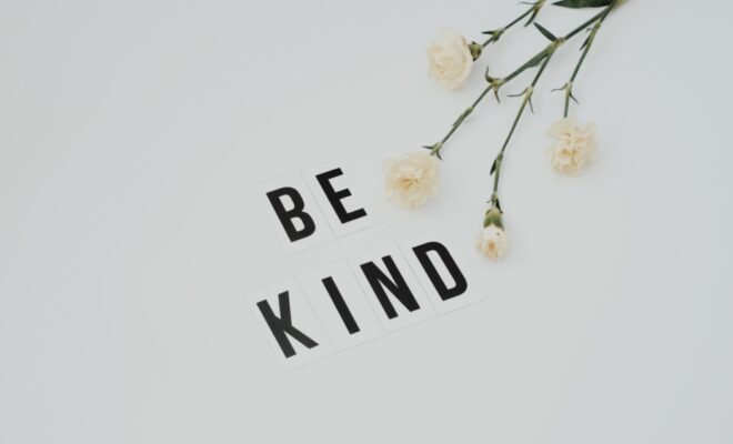 the words be kind in black print on a white background next to cut flowers
