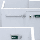 white walls forming a maze with green exit signs white concrete stairs with no people