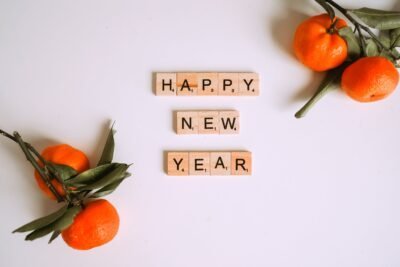 words Happy New Year spelled in wooden tiles with oranges and branches in the corners
