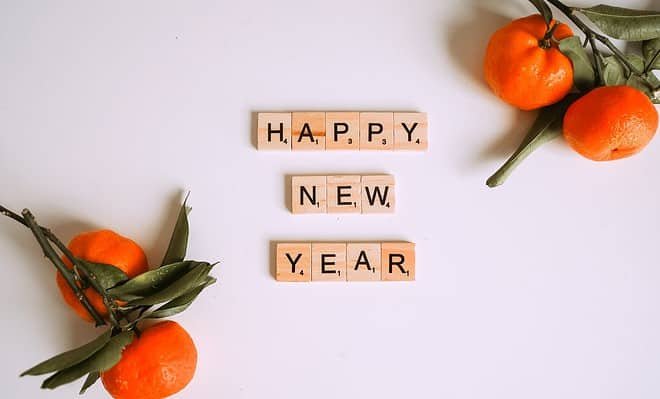 words Happy New Year spelled in wooden tiles with oranges and branches in the corners