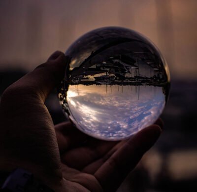Hand holding a glass ball with a revrese image of the sky and a boat dock