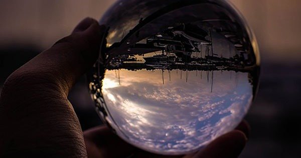 Hand holding a glass ball with a revrese image of the sky and a boat dock