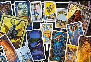 A selection of Tarot cards fading from the Tower, Hierophant, and Six of Swords on the left, the Wheel of Fortune in the center, and the Ten of Cups, Lovers, and the World on the right.
