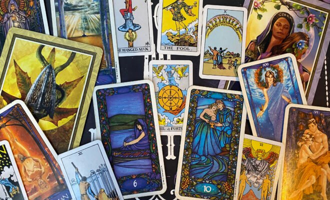 A selection of Tarot cards fading from the Tower, Hierophant, and Six of Swords on the left, the Wheel of Fortune in the center, and the Ten of Cups, Lovers, and the World on the right.