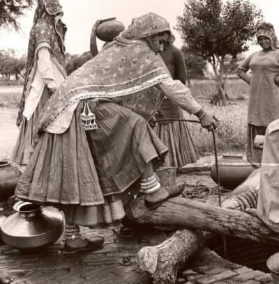 Photograph of 1950s India village women dressed in traditional clothes collecting water at the village well.