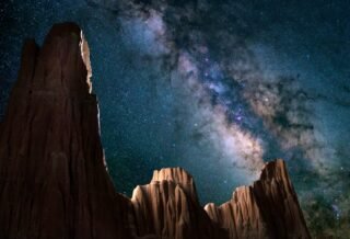 Sheer rocky cliff faces rise up and pierce the night sky. Overhead, a bright band of stars splits the sky.