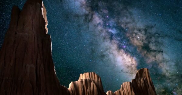 Sheer rocky cliff faces rise up and pierce the night sky. Overhead, a bright band of stars splits the sky.