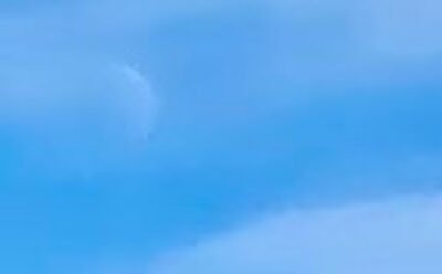The image is of daytime waning crescent, barely visible in a white cloudy sky