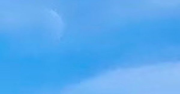 The image is of daytime waning crescent, barely visible in a white cloudy sky