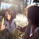 A woman sitting in a field looking at her reflection in a mirror