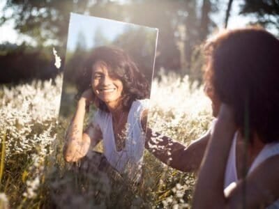 A woman sitting in a field looking at her reflection in a mirror