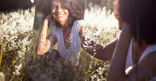 A woman sitting in a field looking at her reflection in a mirror