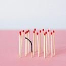 a burnt match within a group of fresh matches on a pink and white background