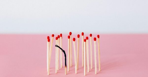 a burnt match within a group of fresh matches on a pink and white background