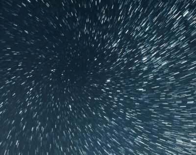 Stars trails along the periphery blur against the dark background of deep space creating a cosmic tunnel to travel through.