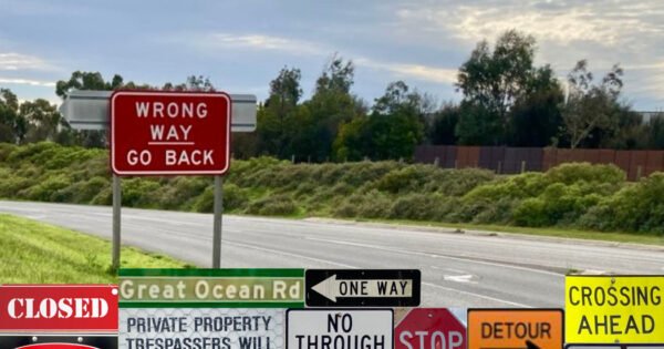 The image is of an empty road, and road sign saying, 'Wrong Way, Go Back", and along the lower part of the image, there numerous other roads signs