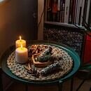two lit candles and three bundles of sage on a round table next to two chairs and a bookshelf