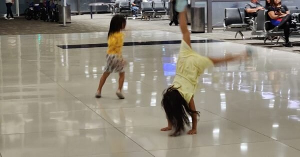 Two kids playing in airport. One running and one doing a handstand.