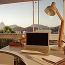 White desk with a laptop and opened notebook in front of a big window with a view of mountains and sunlight.