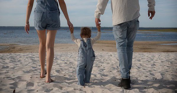 parents walking on the beach with their child. View from behind. Walking towards the water.