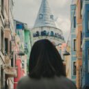 A woman with short dark hair standing in a street with colorful buildings in Istanbul, Turkey and looking at the Galata tower.