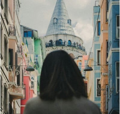 A woman with short dark hair standing in a street with colorful buildings in Istanbul, Turkey and looking at the Galata tower.