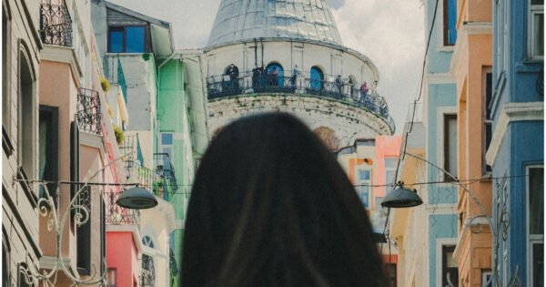 A woman with short dark hair standing in a street with colorful buildings in Istanbul, Turkey and looking at the Galata tower.