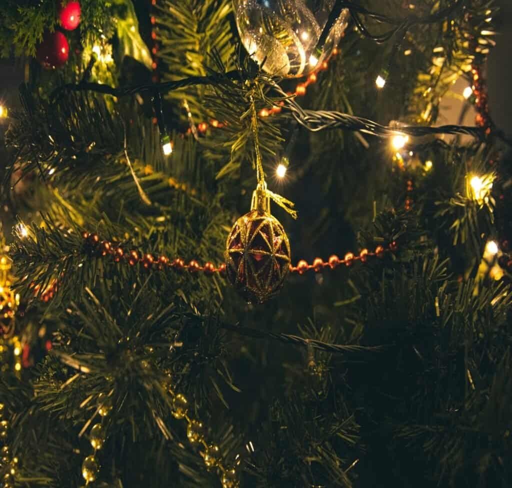 Pine tree branches strung with gold beads and glass ornaments lit by white lights.