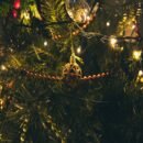 Pine tree branches strung with gold beads and glass ornaments lit by white lights.