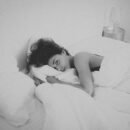 Woman laying in bed covered with white blanket.