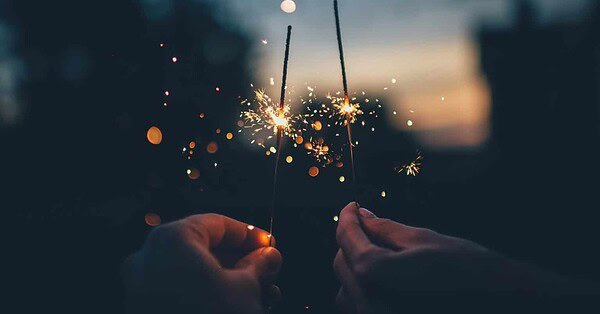 Two hands holding two burning sticks