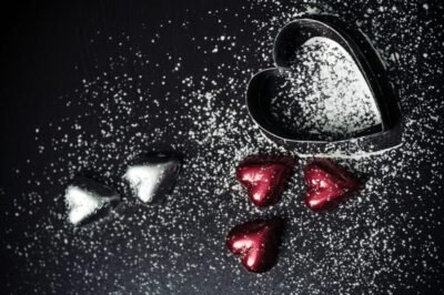 Chocolate wrapped hearts surrounded by powdered sugar and a metal heart cookie cutter