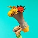 Megaphone with flowers held in one hand on blue backdrop.