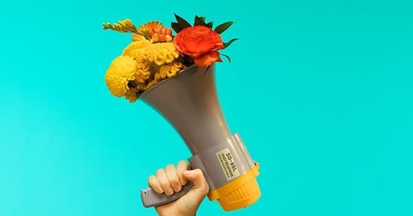 Megaphone with flowers held in one hand on blue backdrop.