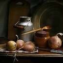 Four fresh onions on a vintage kitchen table with a milk can, jar, spoon, knife, and cookbooks
