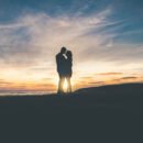 Man and woman embracing each other in front of a sunset.